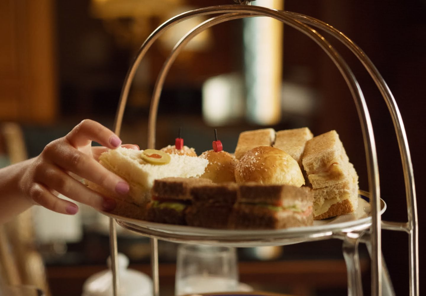 A small hand grabs for a tea sandwich on the Afternoon Tea tray.