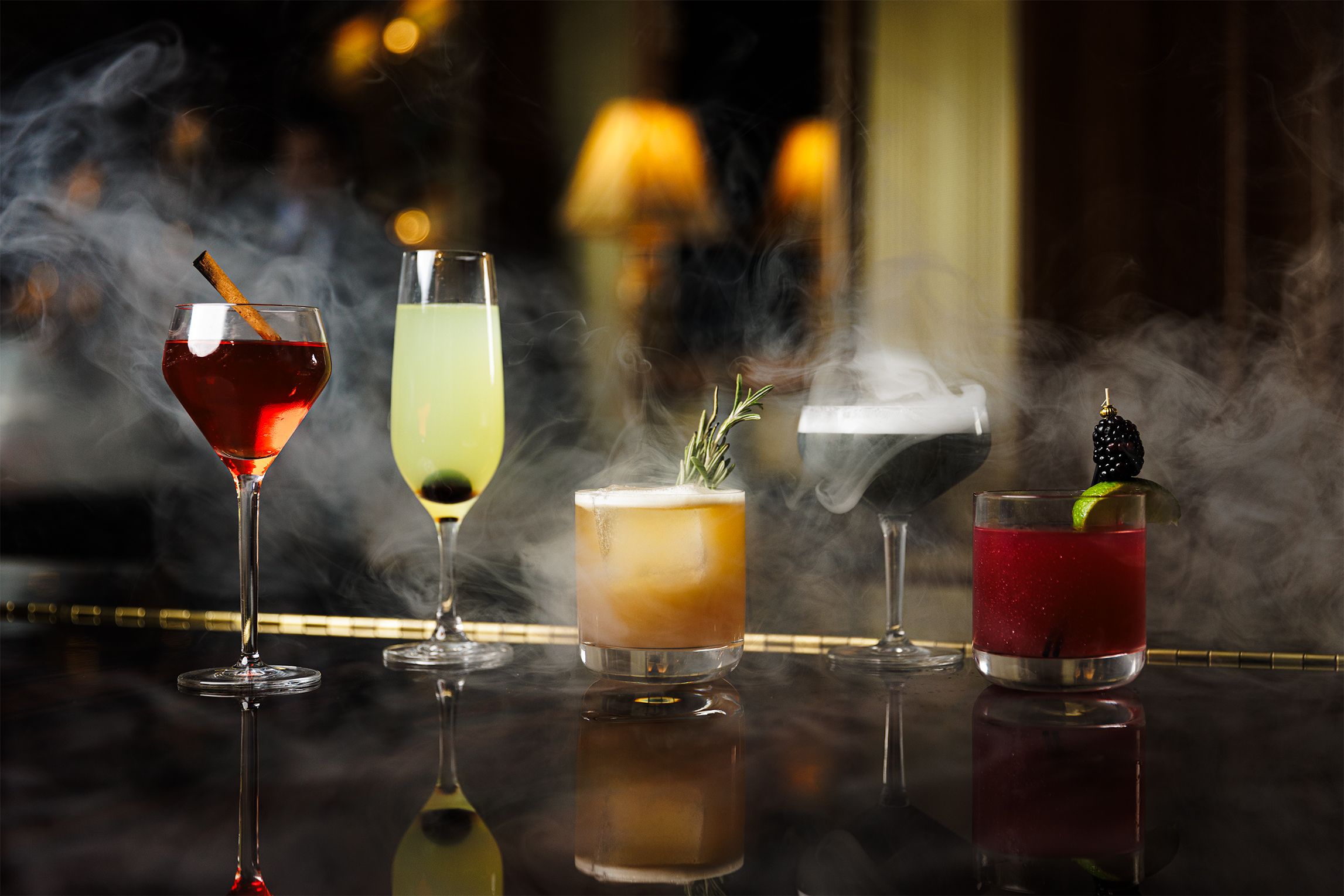 Multiple cocktails on a bar with smoke behind them