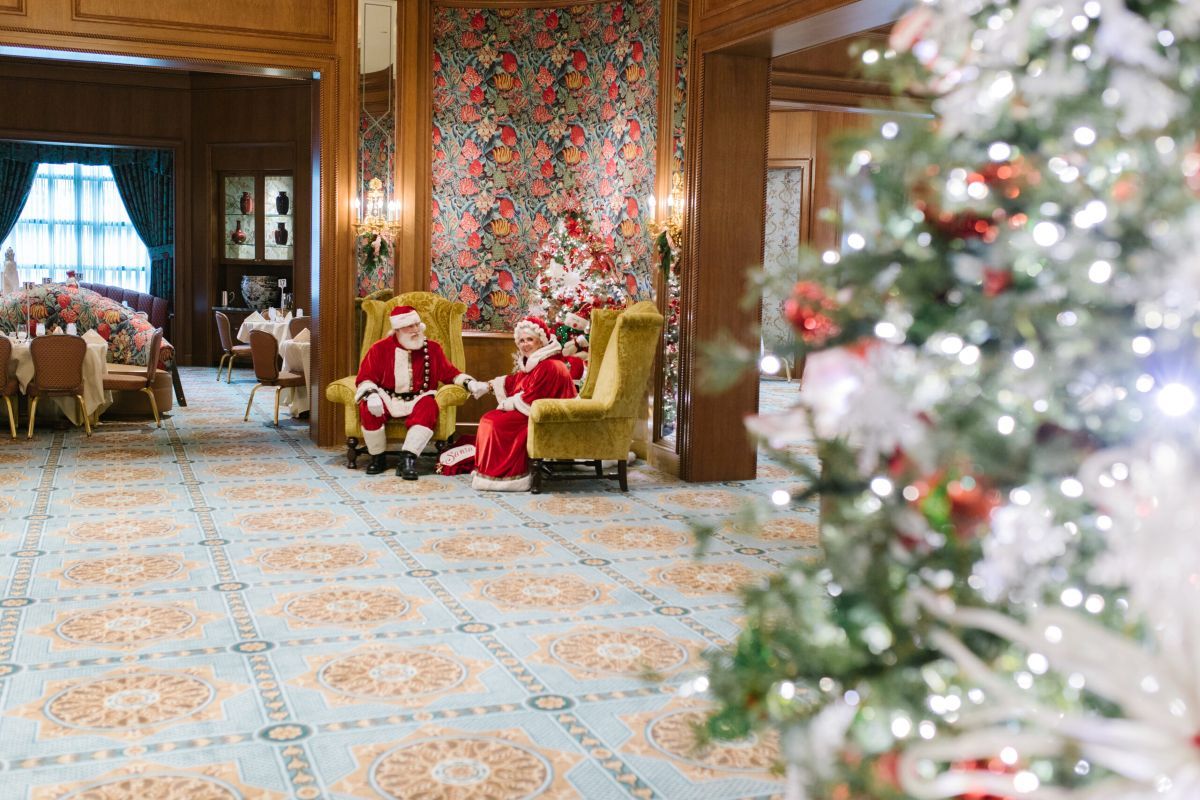 Santa and Mrs. Clause sitting in chair by a Christmas tree