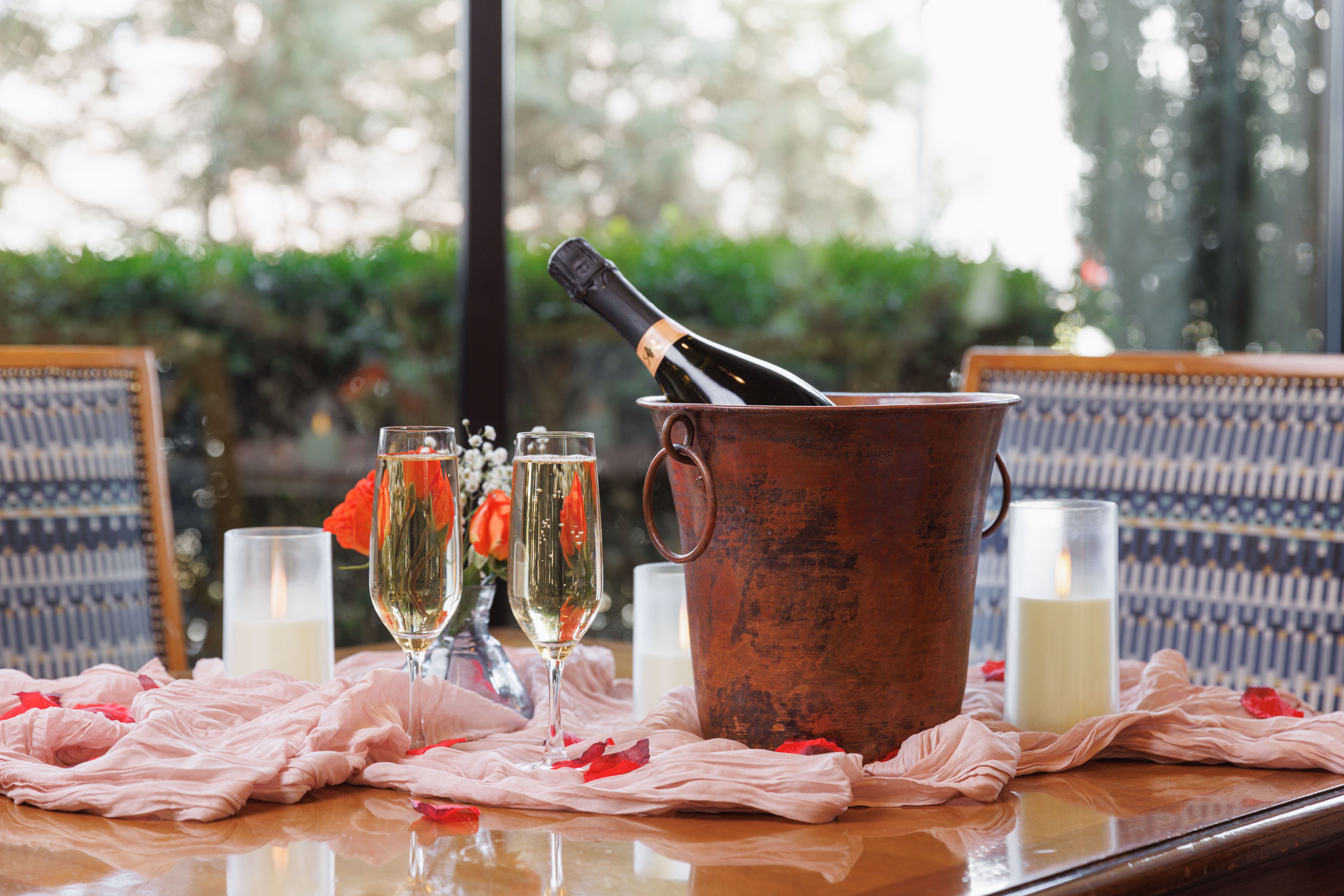 Two glasses of champagne with a bottle in a chiller with rose petals on the table