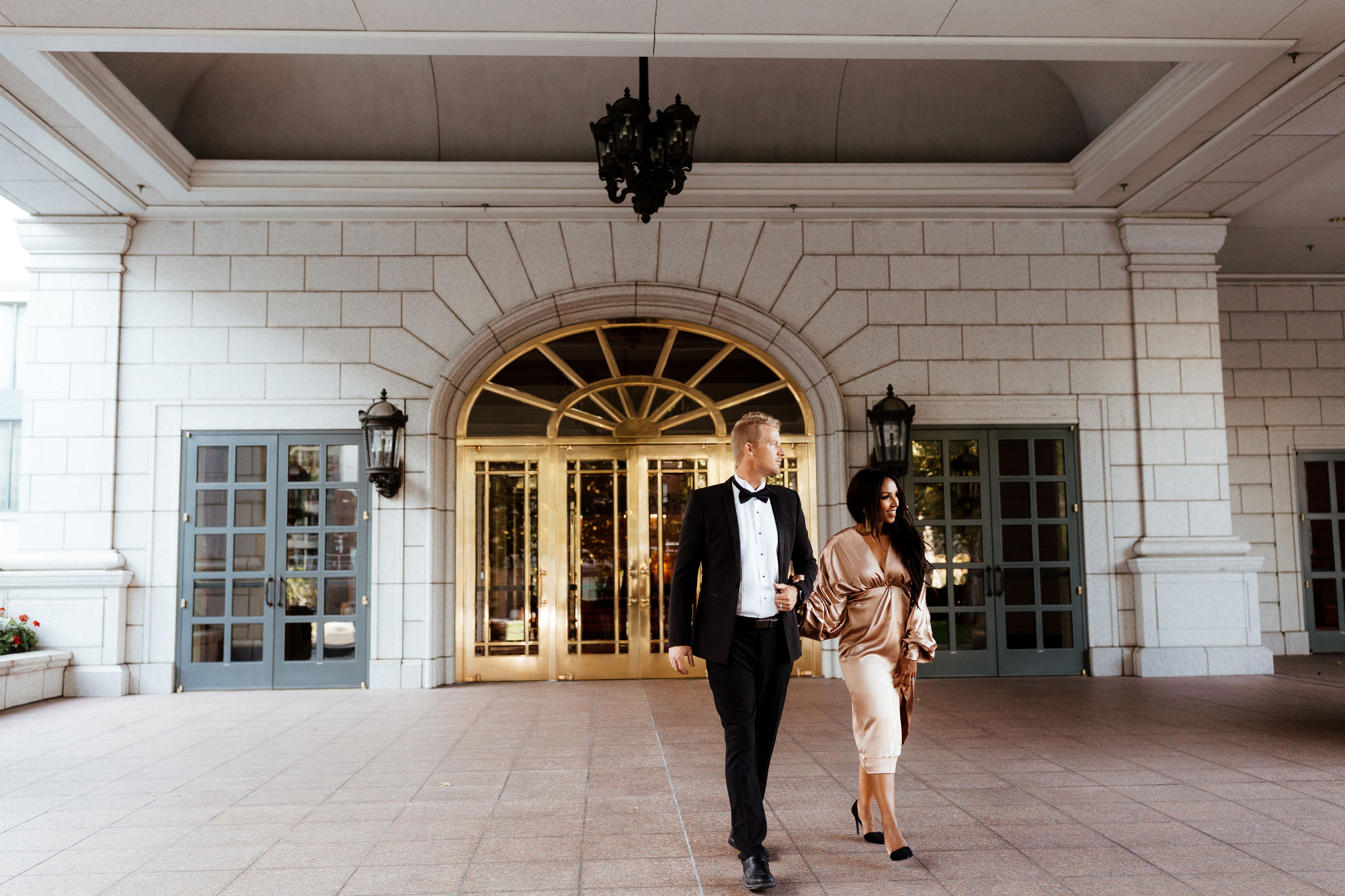 A couple standing in front of gold doors dressed formal